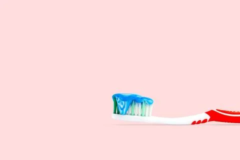 Blue and white toothpaste on a toothbrush isolated on pink color background. Фото