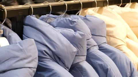 Blue and white winter down jackets hanging on hangers in the store close-up Stock Footage 257736452
