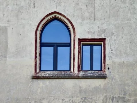 Blue arched window with weathered red trim set into cracked plaster wall, s.. Stock Photos