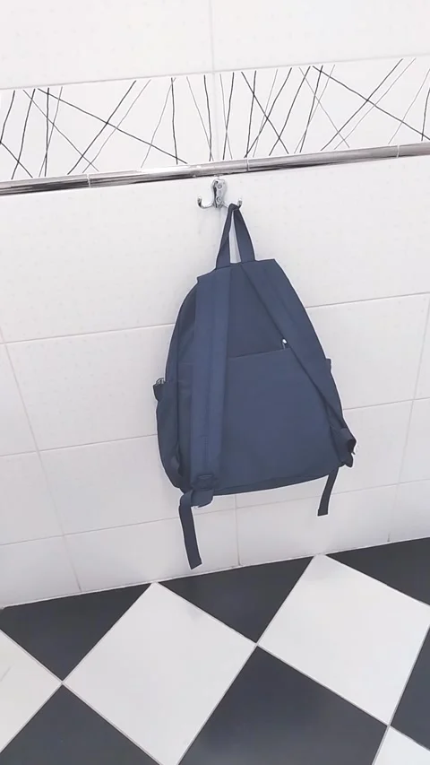 Blue backpack hanging from wall hook above black and white checkered floor Stock Footage 346933227