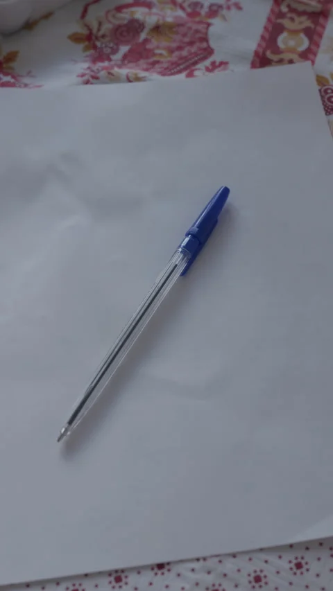 Blue ballpoint pen resting on blank white paper over patterned fabric surface Stock Footage 344824039