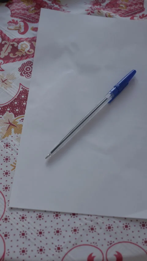 Blue ballpoint pen resting on blank white paper over patterned fabric background Stock Footage 344825580