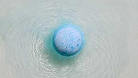 Blue bath bomb ball dissolves in water with white foam bubbles. Cosmetic product Stock Footage 163207761
