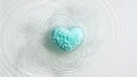 Blue bath bomb ball in the shape of a heart dissolves in water with white foam Stock Footage 255676717