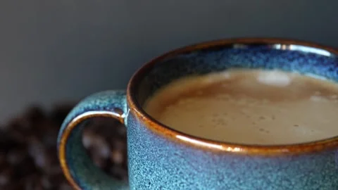 A blue beautiful cup of coffee on a table with coffee grounds on turn table, on Stock Footage 243294649