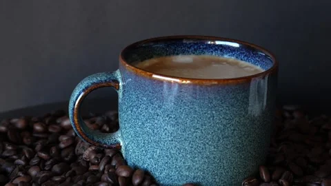 A blue beautiful cup of coffee on a table with coffee grounds on turn table, on Stock Footage 243295143