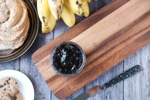 Blue berry jam in a container with bread and banana on table Stock Photos