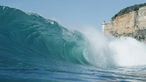 Blue big wave breaking with lighthouse and cliff in the background 4K Stock Footage 128508499