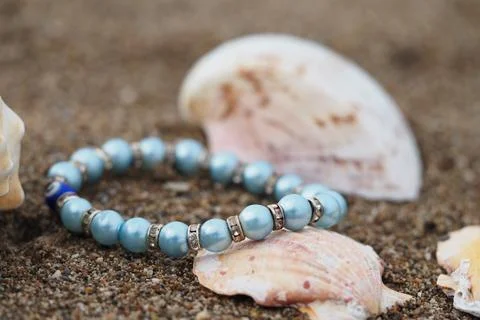 Blue bracelet on sandy beach with shells around Stock Photos