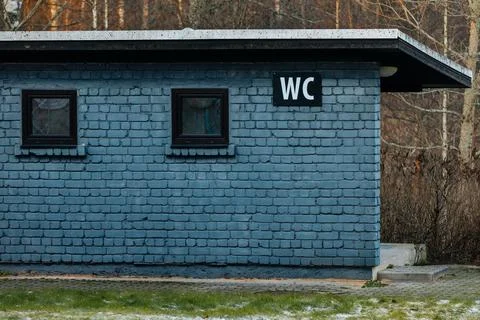 Blue brick building with two windows and a prominent WC sign, surrounded by.. Stock Photos