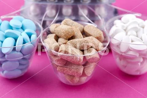 Blue brown and white pills in graduated glass on pink background Stock Photos