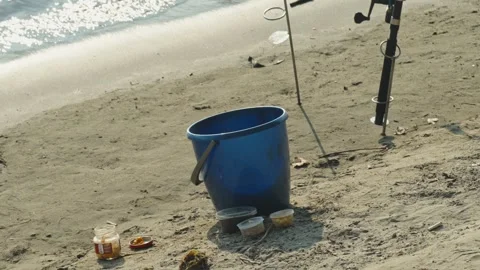 A blue bucket and bait jars stand on a sandy beach Stock Footage 339629013