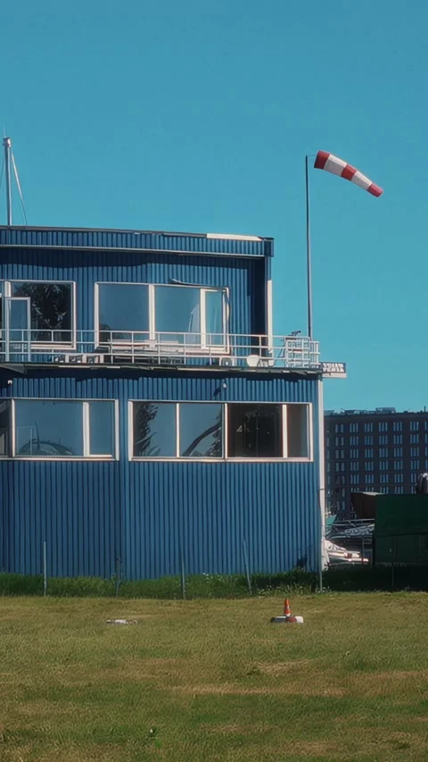 Blue building with large windows and a red and white windsock on a clear day, Stock Footage 329201816