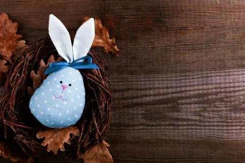 Blue Bunny Easter egg handmade with pretty face lying in a nest on a wooden b Stock Photos