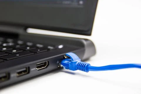 Blue cable network connection to a Lan port of laptop computer on white table Stock Photos