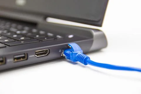 Blue cable network connection to a Lan port of laptop computer on white table 库存照片
