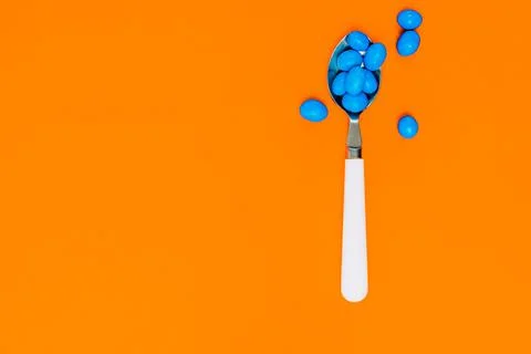 Blue candies inside white spoon on orange background. assortment of candies Stock Photos