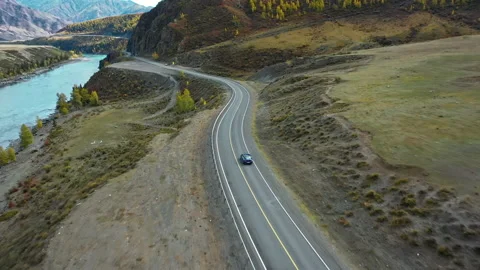 Blue car drives along the road in the mountains along the river. Coupe. Aerial Stock Footage