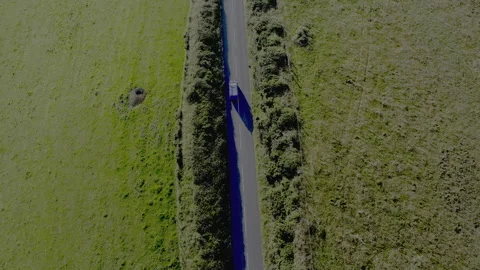 A blue car is driving down a road in a grassy field Stock Footage 298281018