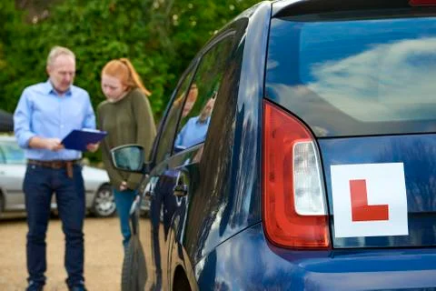 Blue Car with Learner Driver Sign with Driving Student and Teacher in Backgro Stock Photos