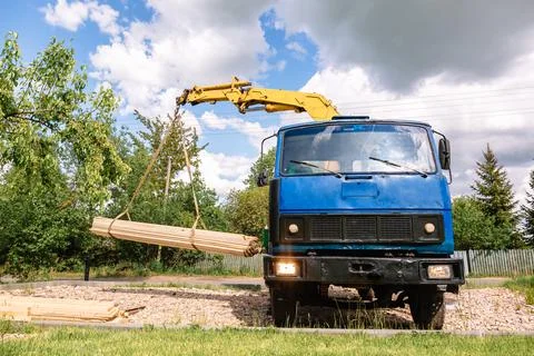 A blue cargo loader with a manipulator unloads the delivered building materia Stock Photos