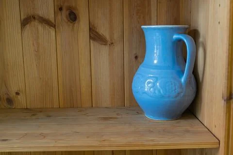 A blue ceramic pitcher sits on a sturdy wooden shelf in an indoor space Foto stock