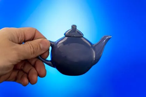 Blue ceramic teapot for making tea in your hand on a blue background Stock Photos