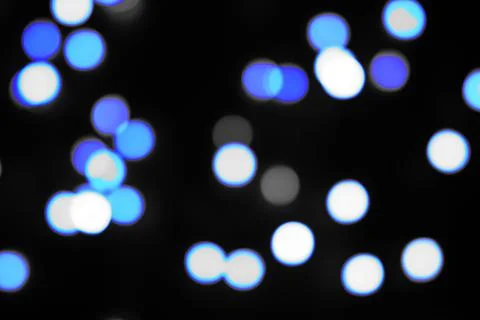 Blue circle bokeh lights blur the pitch dark background. Stock Photos
