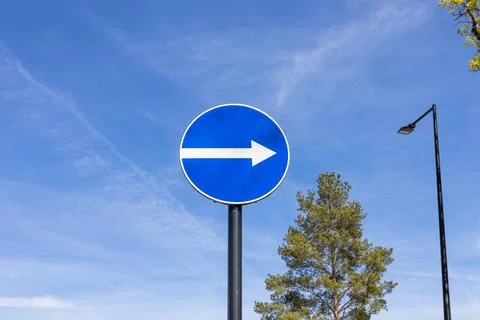 Blue circular traffic sign with white arrow pointing right Stock Photos
