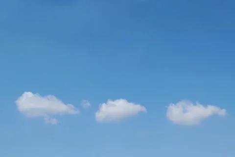 In the blue clear sky float three small Cumulus clouds. Stock Photos