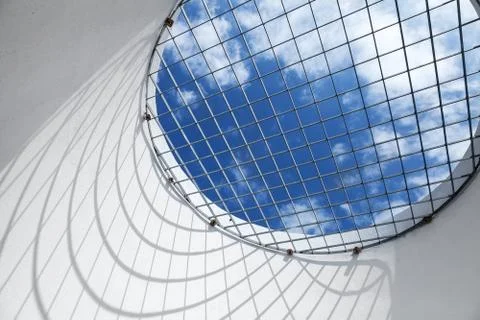 Blue cloudy sky behind the round window with metal grid Stock Photos