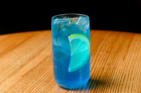 Blue cocktail with lime slice served in a tall glass on wooden table Stock Photos
