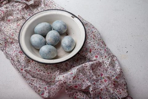 Blue colored Easter eggs in white bowl on purple fabric with flowers pattern. Stock Photos