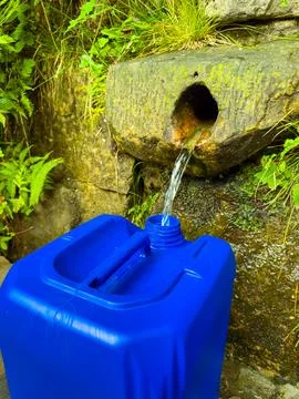 A blue container beneath a clear spring captures fresh water flowing from a r Foto stock