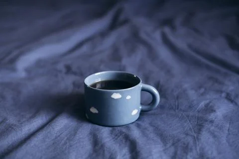 Blue cup with cloud pattern on blue bed, perfect for cozy morning routine. Stock Photos