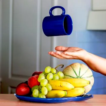 Blue cup, floating on a set of fruit with a woman hand, in a kitchen Stock Photos