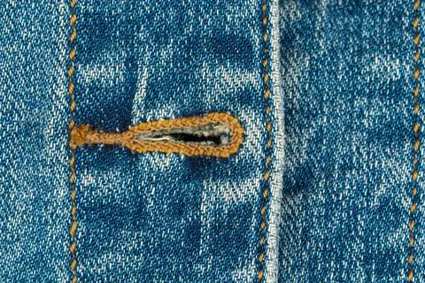 Blue denim fabric texture with buttonhole and orange stitching Stock Photos