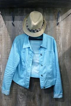A blue denim jacket and a hat are hanging on a hanger Stock Photos