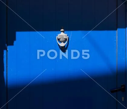 Blue door with knocker in sunlight and shadow Stock Photos