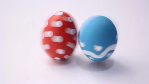 Blue dotted Easter egg spins and hits red egg with polka dots on white table Stock Footage 257582096