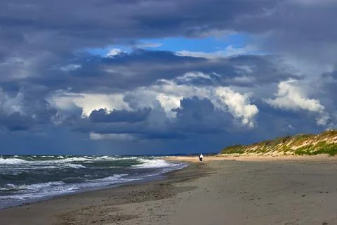 Blue dramatic clouds and sunbeams break through over the beach Stock Photos