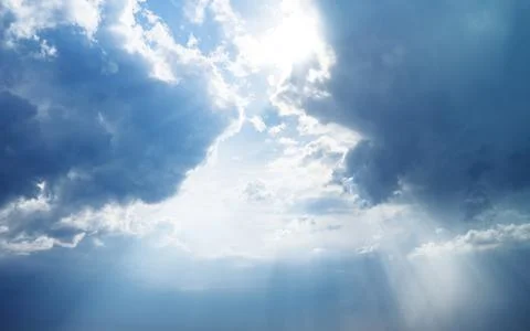Blue dramatic sky background with clouds and sun rays coming out. Stock Photos