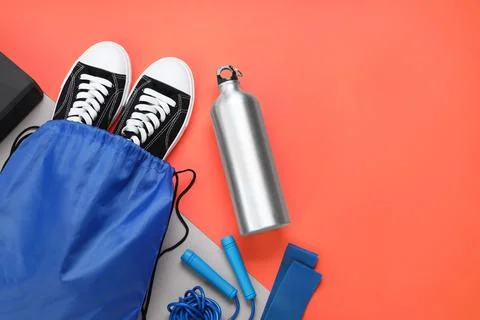 Blue drawstring bag, thermo bottle, skipping rope and sneakers on red backg.. Stock Photos