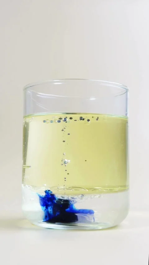 Blue drop dispersing in yellow liquid inside a glass 動画素材 331774305