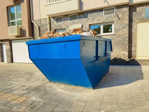 A blue dumpster is placed outside a building. It is filled with bricks and co Stock Photos