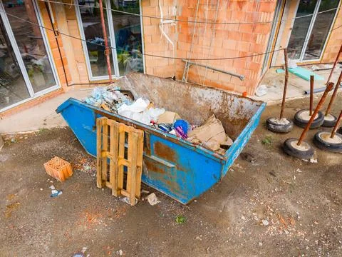 A blue dumpster stands at a construction site filled with trash and materials Stock Photos