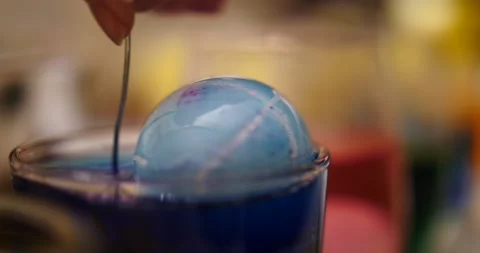 Blue dyed Easter eggs being lifted out of glass full of blue dye Stock Footage 151503576
