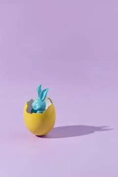 Blue Easter bunny in a yellow eggshell on a pink background. Easter minimal a Stock Photos
