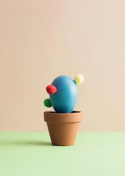 Blue Easter egg arranged like a potted cactus on a green and pink background. Stock Photos