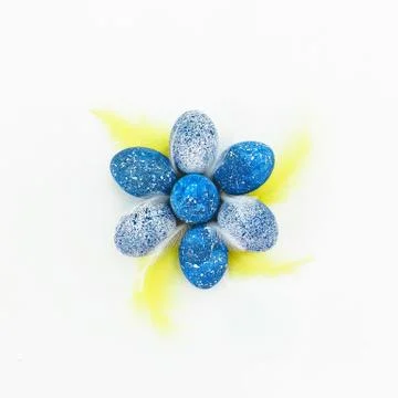 Blue Easter eggs with bright yellow feathers on white background. Flat lay, t Stock Photos